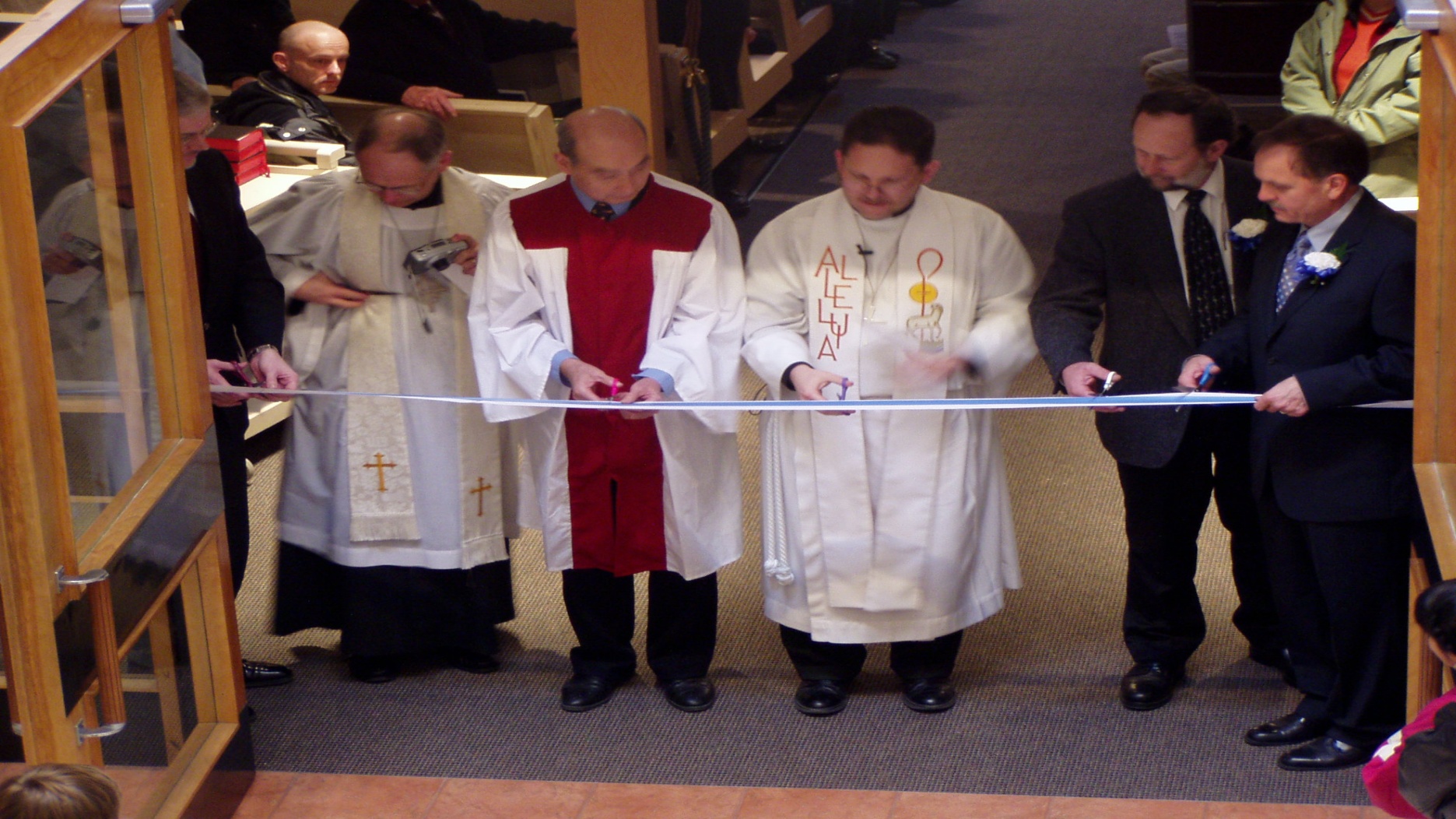 A 2003 photograph of the dedication and ribbon-cutting ceremony at Trinity Lutheran Church in Richmond, BC. Pastors and laity are pictured at the entrance to the sanctuary, at the connection point to the new narthex, symbolizing the official opening of the new multi-use facility and completion of renovations to the 1964 church building.