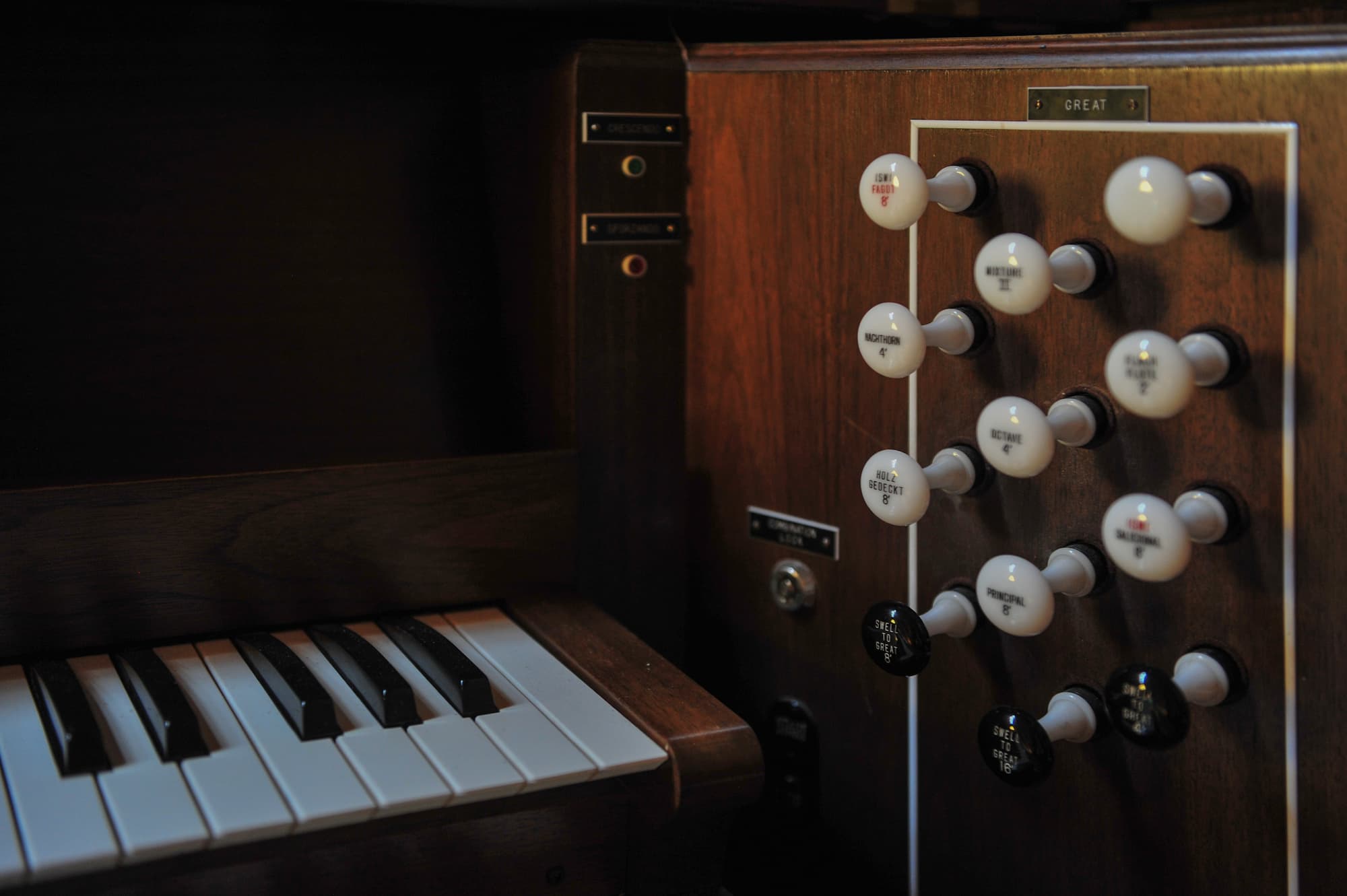 A detailed photograph of the Wicks pipe organ console at Trinity Lutheran Church in Richmond, BC. The image shows the rhythmic arrangement of white drawknobs, a portion of the keyboard, and the fine woodwork of the organ's dark wood cabinet.