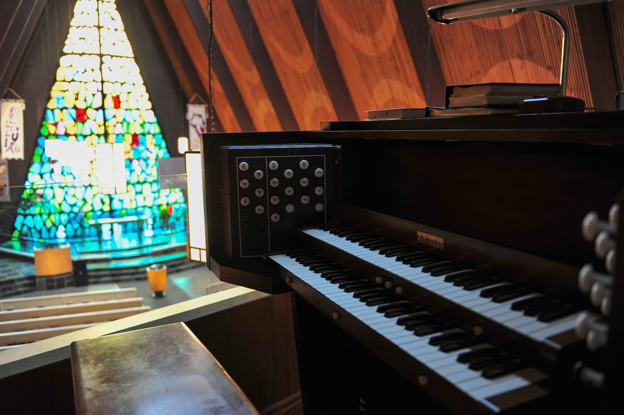 View from the choir loft of the Wicks pipe organ console at Trinity Lutheran Church, Richmond. The background reveals the altar, pulpit, and font before a vibrant A-frame stained-glass window